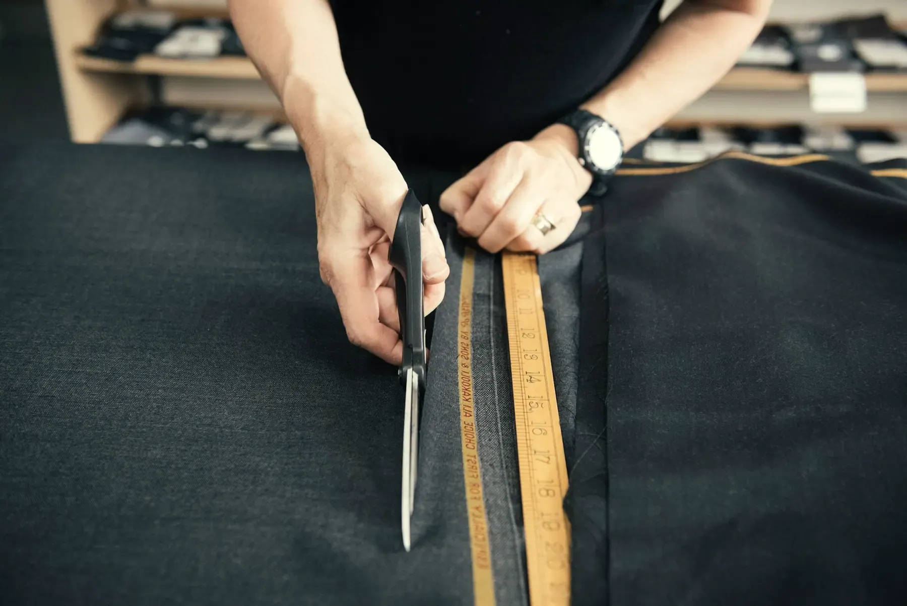Scissors cutting dark fabric along a wooden ruler on a cutting table