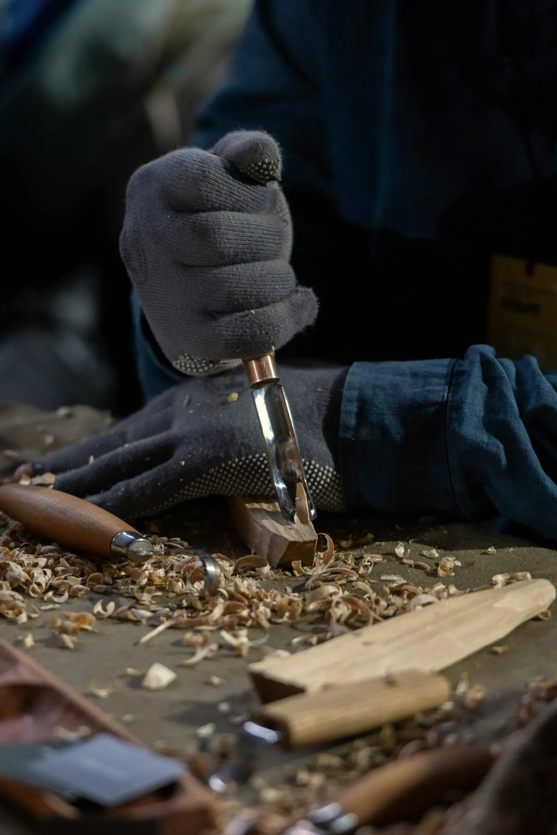 Hands carving a piece of wood with a chisel, with shavings on the bench