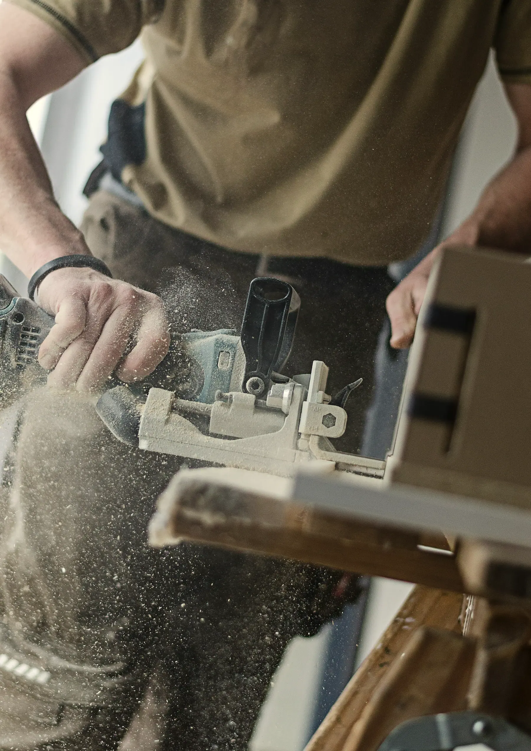 A biscuit joiner cutting a slot in a wooden board, with fine dust in the air
